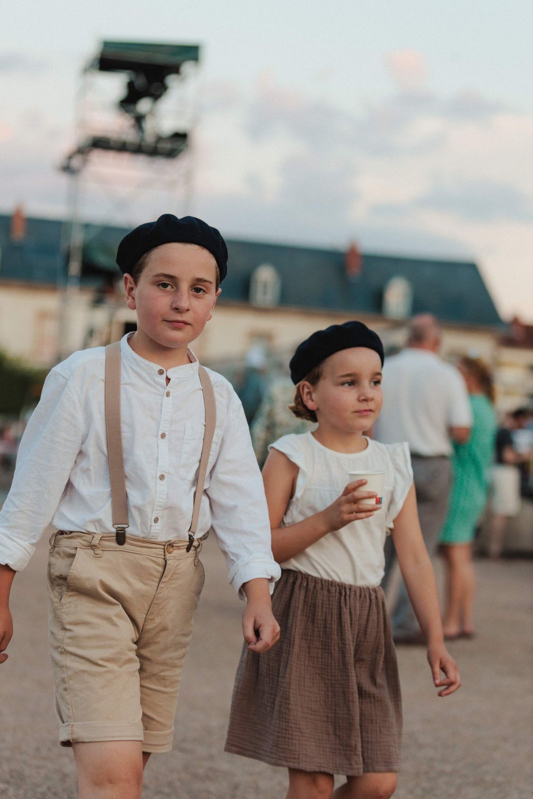 Deux enfants en béret et bretelles marchent au crépuscule