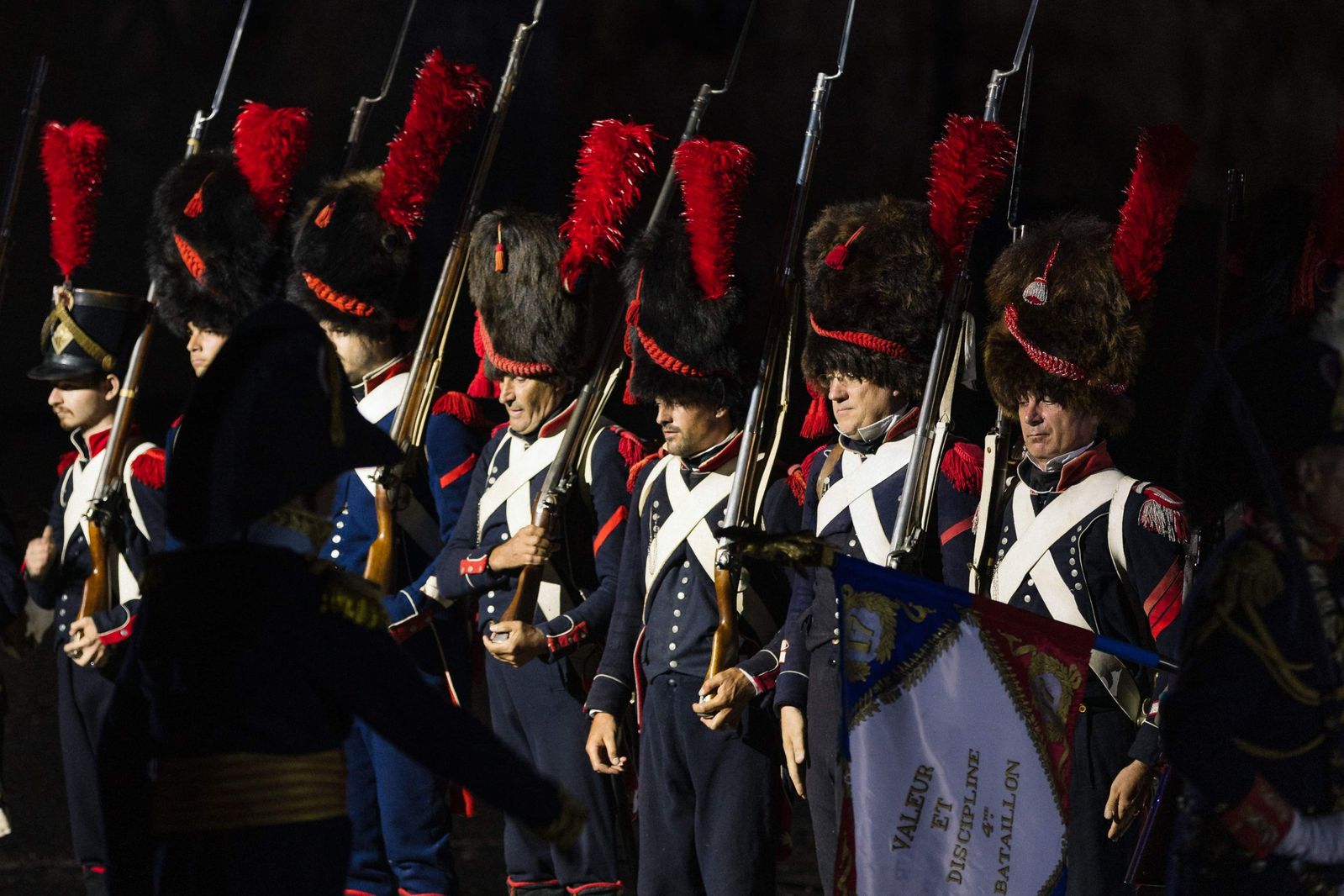 Des grenadiers en grand uniforme et bonnet à poil, au garde-à-vous devant leur drapeau