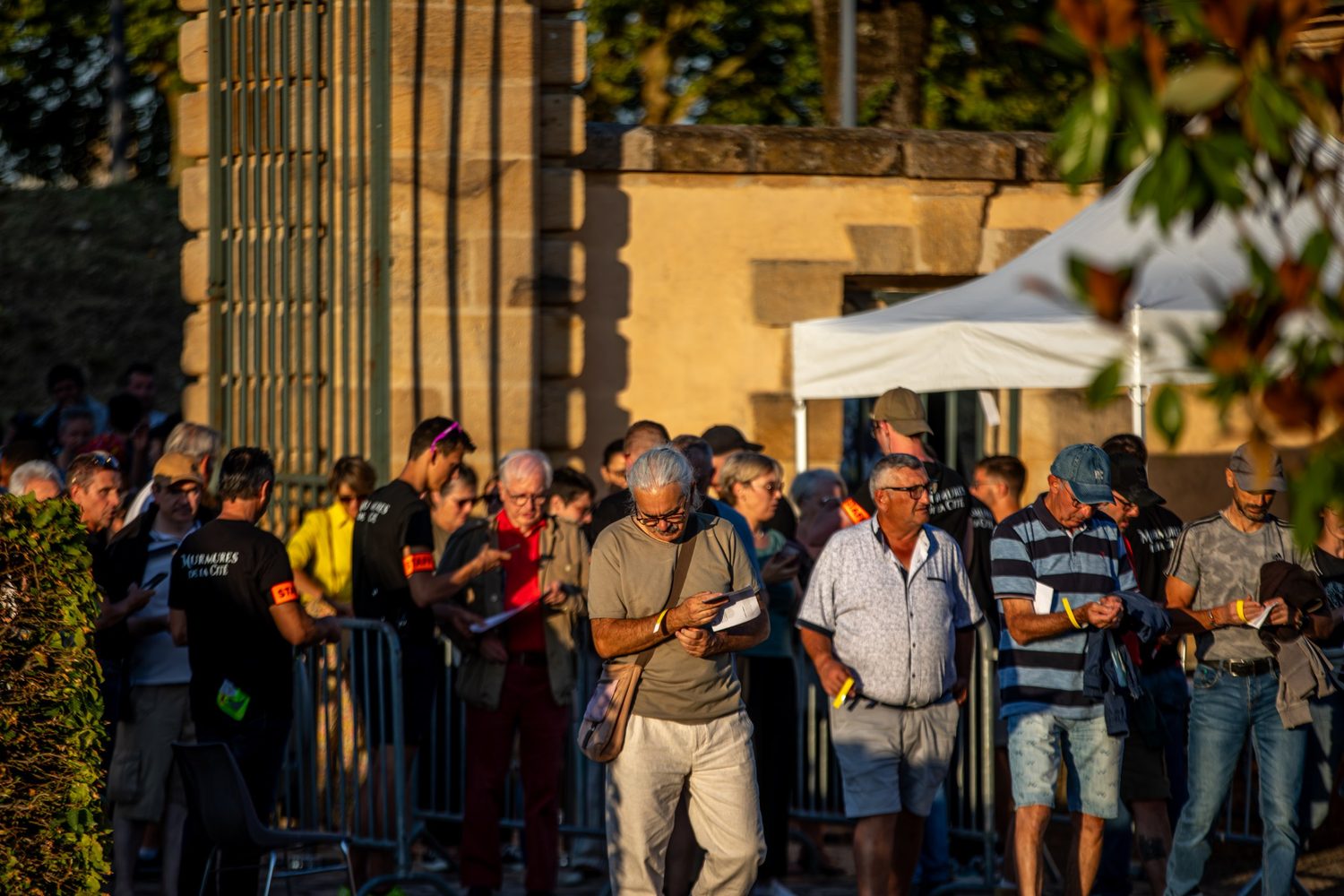 Des spectateurs patientent en file, bracelet au poignet, au coucher du soleil