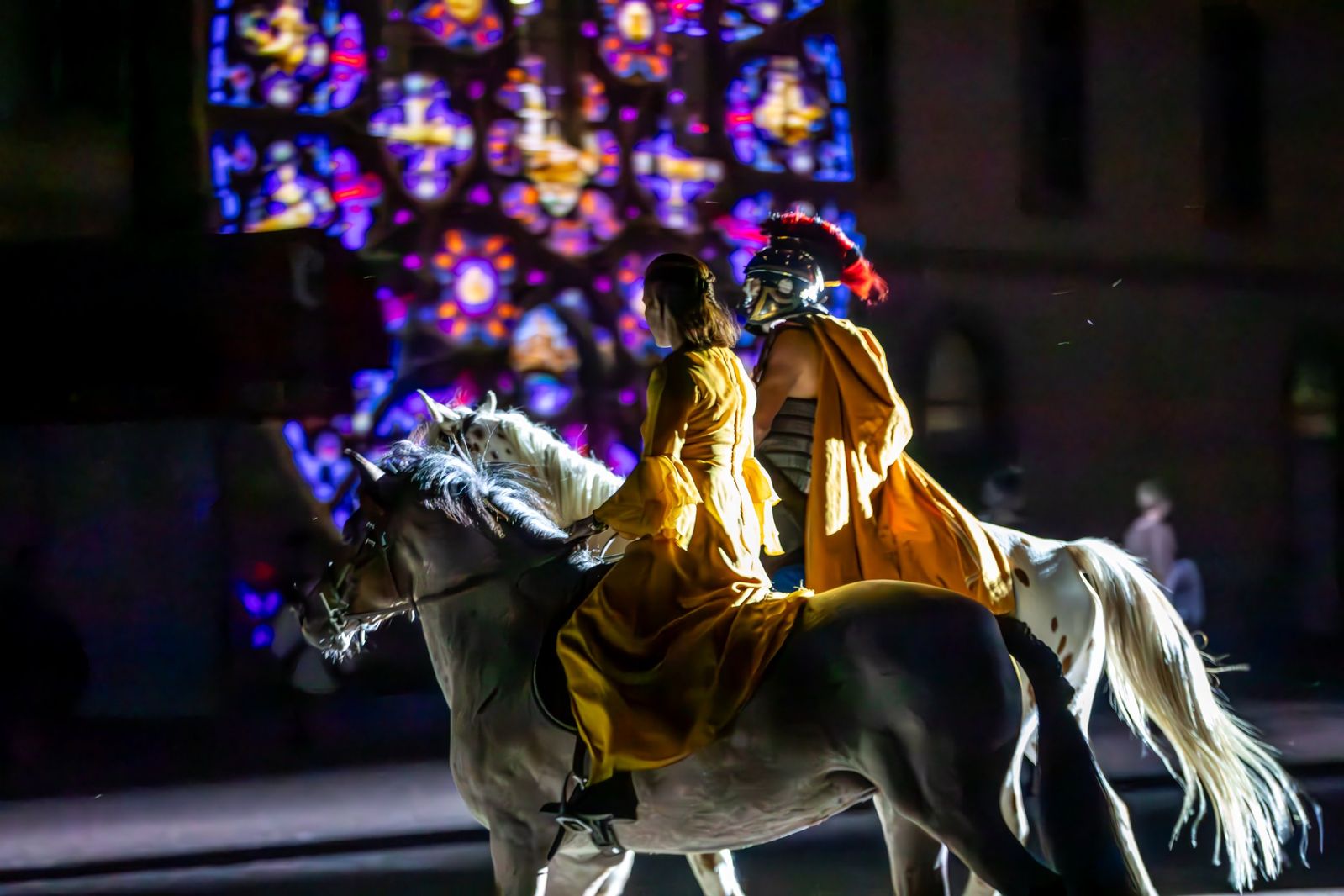 Une cavalière en robe jaune et un légionnaire romain à cheval devant un vitrail projeté