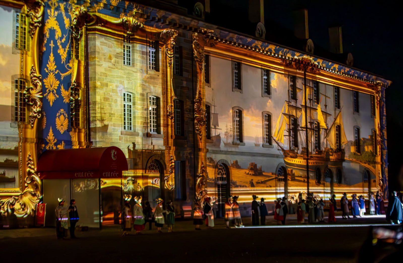 Une façade aux dorures et à un grand navire projetés, devant la foule des figurants